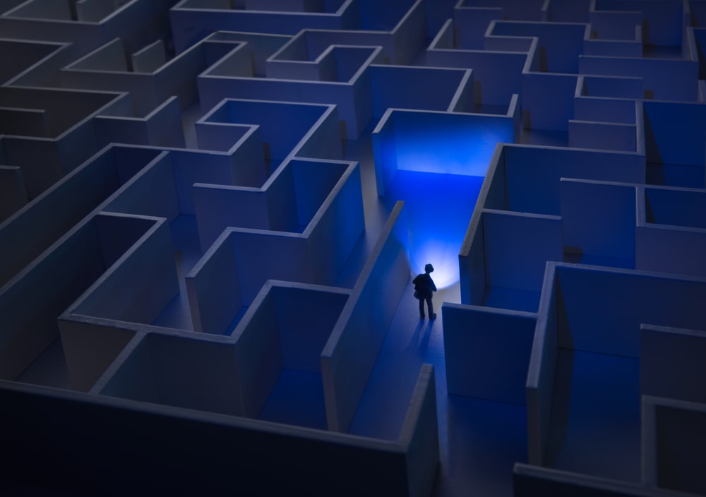 A picture of a person searching through a blue maze with a tiny flash light trying to find meaning